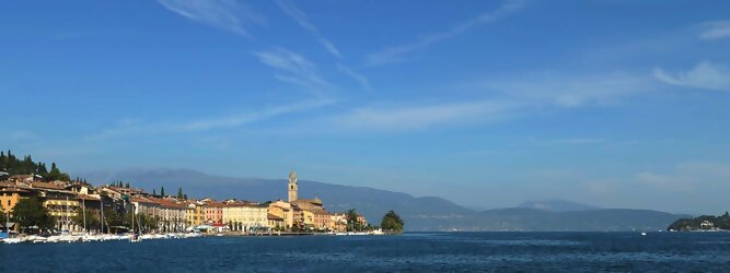 Trip Highlights beliebte Urlaubsziele am Gardasee -  Mit einer Fläche von 370 km² ist der Gardasee der größte See Italiens. Es liegt am Fuße der Alpen und erstreckt sich über drei Staaten: Lombardei, Venetien und Trentino. Die maximale Tiefe des Sees beträgt 346 m, er hat eine längliche Form und sein nördliches Ende ist sehr schmal. Dort ist der See von den Bergen der Gruppo di Baldo umgeben. Du trittst aus deinem gemütlichen Hotelzimmer und es begrüßt dich die warme italienische Sonne. Du blickst auf den atemberaubenden Gardasee, der in zahlreichen Blautönen schimmert - von tiefem Dunkelblau bis zu funkelndem Türkis. Majestätische Berge umgeben dich, während die Brise sanft deine Haut streichelt und der Duft von blühenden Zitronenbäumen deine Nase kitzelt. Du schlenderst die malerischen, engen Gassen entlang, vorbei an farbenfrohen, blumengeschmückten Häusern. Vereinzelt unterbricht das fröhliche Lachen der Einheimischen die friedvolle Stille. Du fühlst dich wie in einem Traum, der nicht enden will. Jeder Schritt führt dich zu neuen Entdeckungen und Abenteuern. Du probierst die köstliche italienische Küche mit ihren frischen Zutaten und verführerischen Aromen. Die Sonne geht langsam unter und taucht den Himmel in ein leuchtendes Orange-rot - ein spektakulärer Anblick.